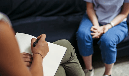 Therapist taking notes during a counseling session with a seated client.