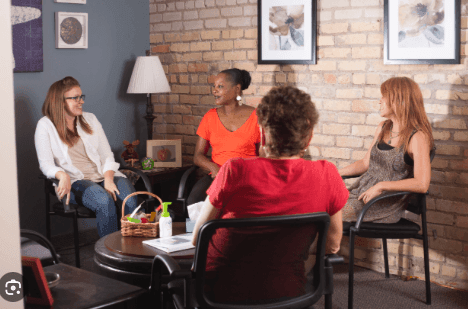 Group of women sitting and talking in a cozy room with brick walls and framed art.